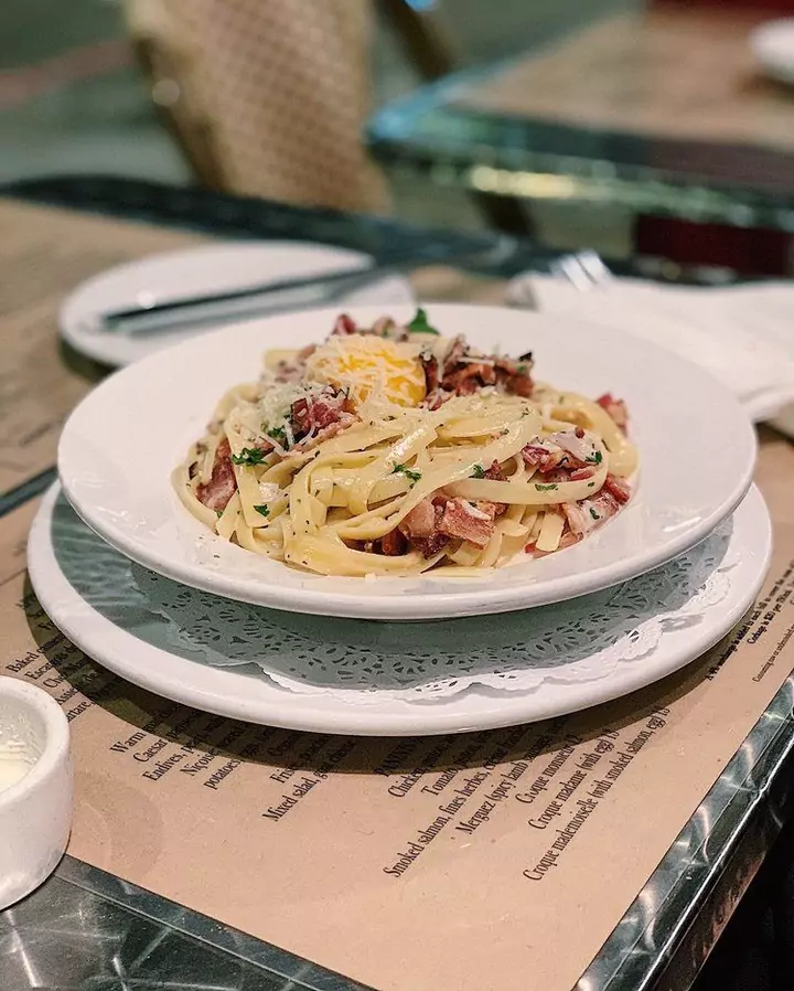 White Bowl filled with homemade spaghetti with pancetta, green herbs, shredded parmesan cheese, and egg yolk