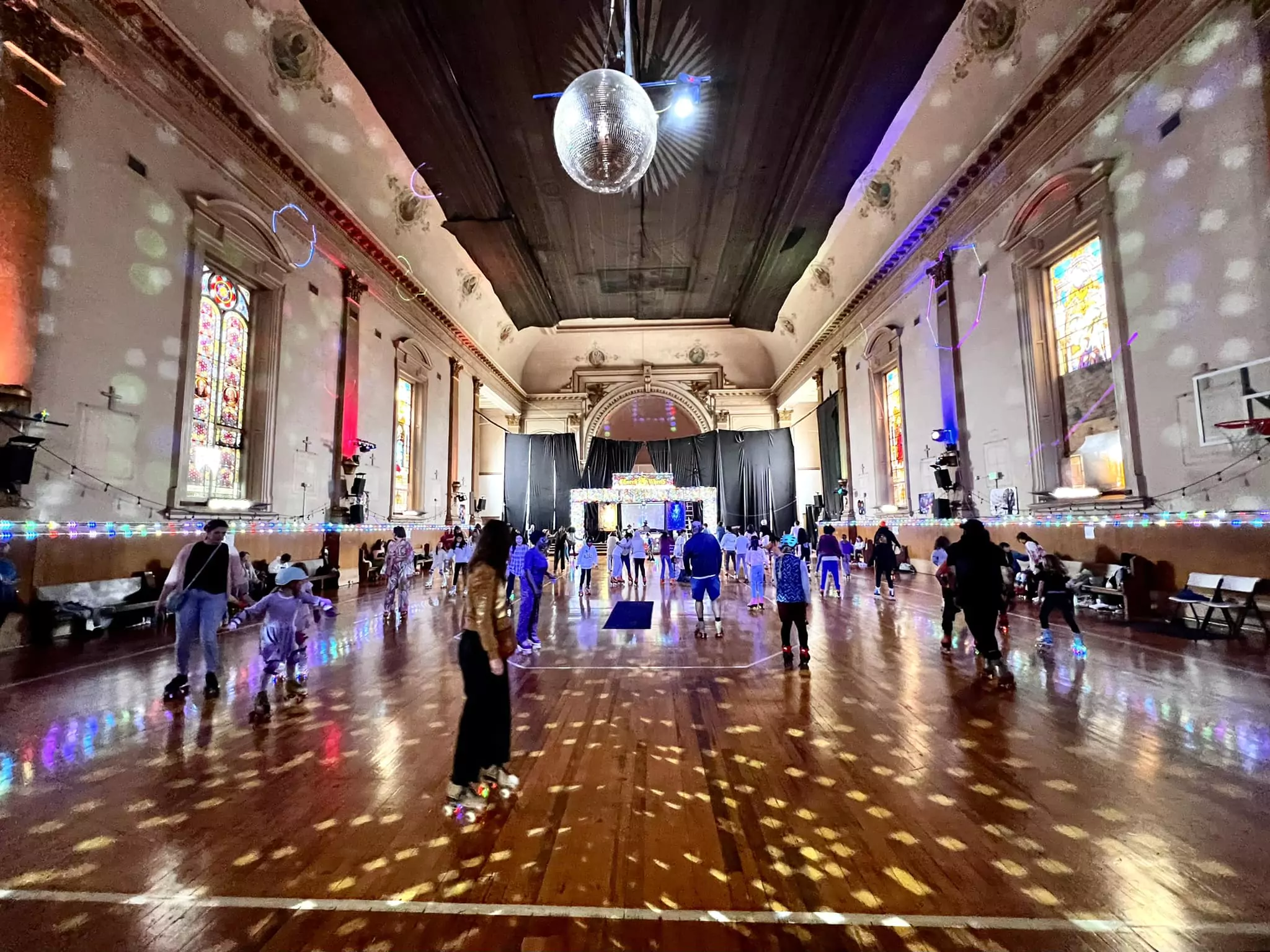 Indoor roller skating rink lit up with circular white strobe lights, a disco ball, and dozens of people skating