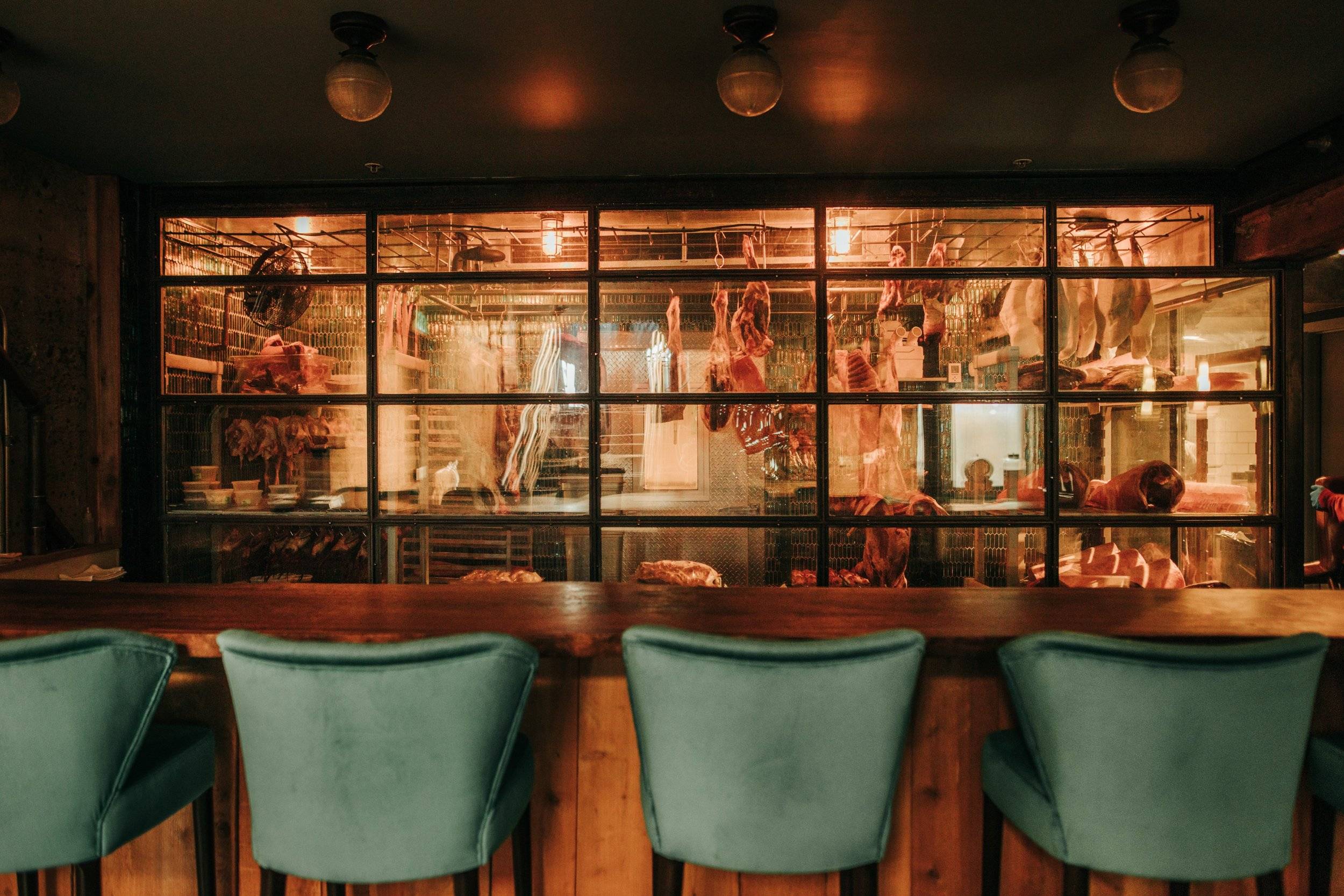 Empty Green Velvet Dining Seats Faced Towards a Meat Storage Room with Hanging Refrigerated Meats at Birdsong